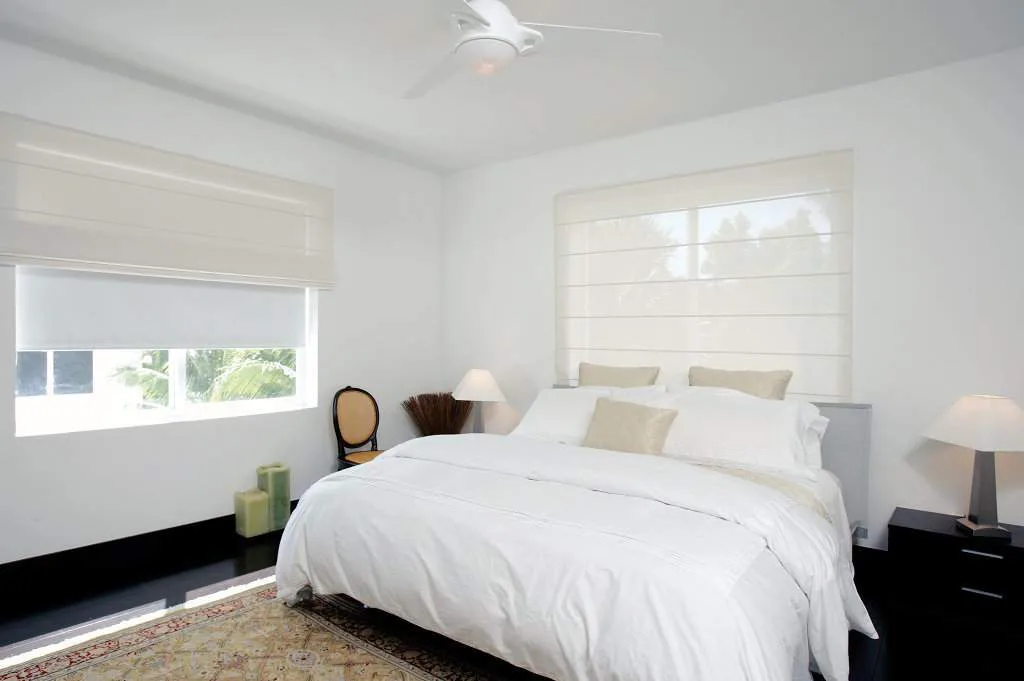 Cortinas enrollables blancas en dormitorio con ventana de guillotina